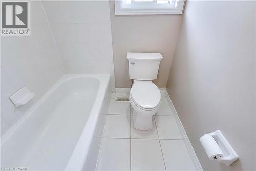 White ceramic tile flooring, bathtub with white tile surround, and a window with natural light - 214 Cloverleaf Drive, Ancaster, ON 