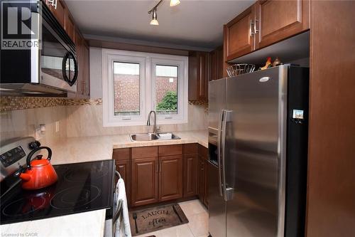 Kitchen with wood-finish cabinetry, stainless steel appliances, a double basin sink, and a tiled backsplash - 154 Ewen Road, Hamilton, ON 