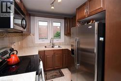 Kitchen with wood-finish cabinetry, stainless steel appliances, a double basin sink, and a tiled backsplash - 