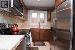 Kitchen featuring wood cabinetry, stainless steel appliances, a tile backsplash, and a window above the sink - 