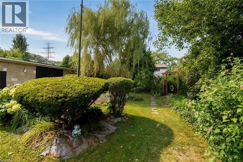 Expansive lawn area with stepping stone path, mature trees, manicured shrubs, and a wood-frame arbor - 154 Ewen Road, Hamilton, ON 