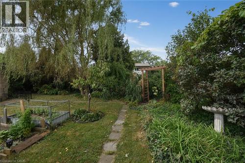 Expansive backyard featuring a stone birdbath, raised garden beds, a mature weeping willow tree, and a wooden arbor - 154 Ewen Road, Hamilton, ON 