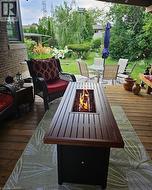 Expansive wooden deck with a built-in fire feature, overlooking a landscaped backyard with mature greenery and a stone patio - 
