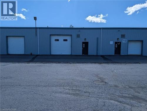 Corrugated metal exterior with multiple roll-up doors, ground-level entry doors, and exterior lighting fixtures - 97 Ardelt Avenue, Kitchener, ON 