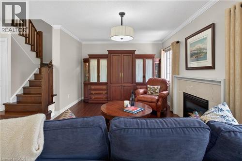 Living area featuring wood-finish flooring, a contemporary fireplace with a light-toned surround, crown molding, and a visible staircase with wood treads and railings - 1347 Brookstar Drive, Oakville, ON 