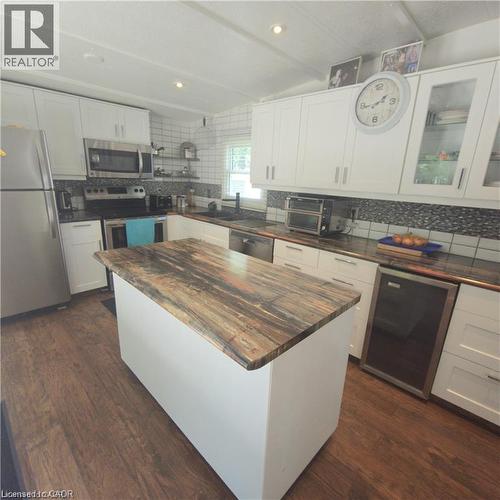 Modern kitchen featuring white cabinetry with glass-front upper cabinets, a substantial island with a rich wood-finish countertop, stainless steel appliances including a double wall oven, granite-styl - 580 Beaver Creek Road Unit# Lot 158, Waterloo, ON 