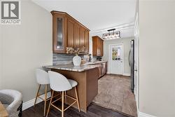 Wood-finish cabinetry with glass accents, stone-look countertop, rectangular tile backsplash, and a modern ceiling fixture - 