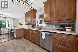 Kitchen featuring wood cabinetry, stone-look countertops, a tile backsplash, and stainless steel dishwasher - 