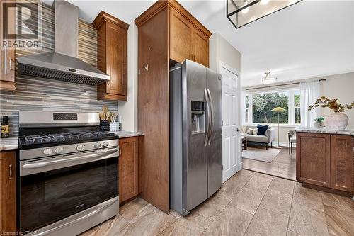 Stainless steel gas range with coordinating ventilation hood, mosaic tile backsplash, wood cabinetry, and stainless steel refrigerator - 176 Avalon Place, Kitchener, ON 