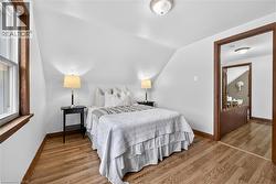 Sloped ceiling room featuring wood-finish flooring, white walls, and a window with wood trim - 