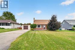 Brick facade residence with a pitched roof, front lawn, mature trees, an attached garage, and a paved driveway - 