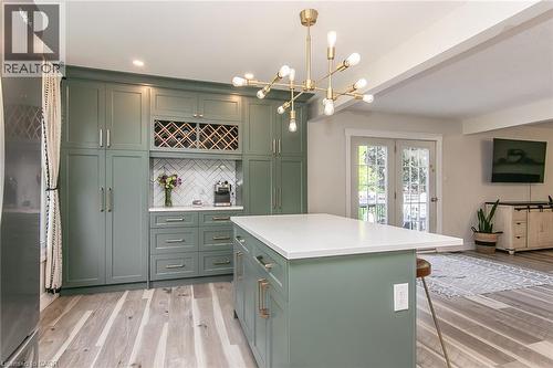 Integrated cabinetry with wine rack, herringbone tile backsplash, large center island with solid surface countertop, and wood-finish flooring - 393 Huron Street, New Hamburg, ON 