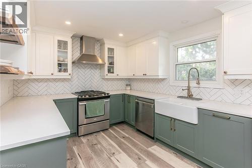 Modern kitchen featuring two-tone cabinetry, stainless steel appliances, a white farmhouse sink, herringbone tile backsplash, and light wood-finish flooring - 393 Huron Street, New Hamburg, ON 