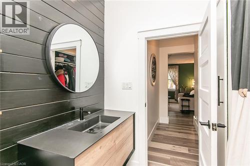Floating vanity with wood-finish cabinetry, integrated basin, matte black faucet, and round mirror - 393 Huron Street, New Hamburg, ON 