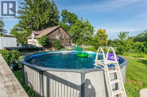 Above-ground swimming pool with an attached ladder, surrounded by green landscaping and mature trees - 393 Huron Street, New Hamburg, ON 