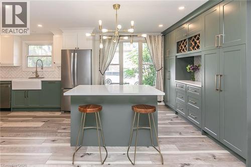Spacious kitchen featuring a central island with a solid surface countertop, wood-finish flooring, a farmhouse sink with a gooseneck faucet, full-height cabinetry, and built-in wine storage - 393 Huron Street, New Hamburg, ON 