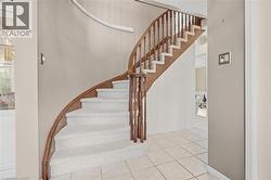 Curved staircase with wood-finish handrail and balusters, carpeted treads, and tiled flooring - 
