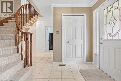 Curved staircase with wood railing, carpeted stairs, tile flooring, crown molding, and a front entry door with decorative glass - 5 Michelle Drive, St. Catharines, ON 