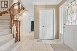Curved staircase with wood railing, carpeted stairs, tile flooring, crown molding, and a front entry door with decorative glass - 