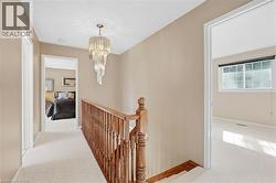 Hallway featuring a crystal chandelier, wood handrail, and light-toned carpeting - 