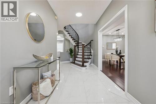 Tiled flooring in a polished finish, curved staircase with dark wood-finish treads and balusters, recessed lighting, and an open doorway to an adjacent room with wood-finish flooring - 154 Falconridge Drive, Kitchener, ON 
