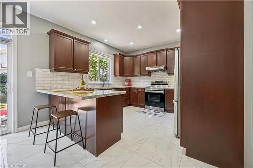 Kitchen featuring wood-finish cabinetry, light-toned countertops, subway tile backsplash, stainless steel appliances, and large format floor tiles - 154 Falconridge Drive, Kitchener, ON 
