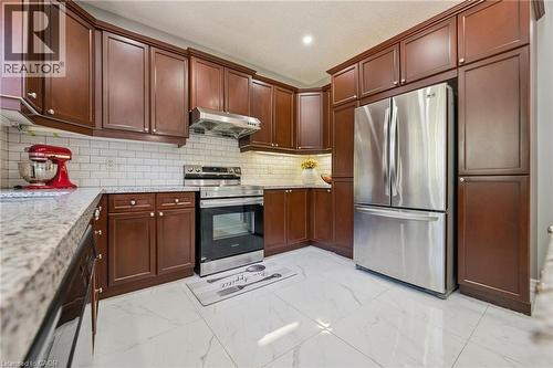 Kitchen featuring stainless steel appliances, dark wood-finish cabinetry, white subway tile backsplash, and light-toned flooring - 154 Falconridge Drive, Kitchener, ON 