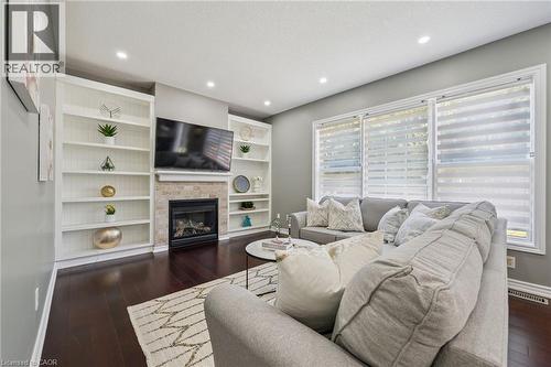 Built-in shelving flanking a natural stone-clad fireplace, recessed lighting, expansive windows, and dark wood-finish flooring - 154 Falconridge Drive, Kitchener, ON 