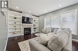 Built-in shelving flanking a natural stone-clad fireplace, recessed lighting, expansive windows, and dark wood-finish flooring - 