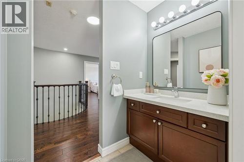 Hardwood flooring, dark wood-finish vanity with drawer and cabinet storage, light-toned countertop, rectangular wall-mounted mirror, and a wall-mounted light fixture with multiple bulbs - 154 Falconridge Drive, Kitchener, ON 