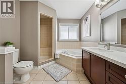 Tiled flooring, built-in shower stall with tiled walls, soaking tub with tiled surround, single vanity with light-tone countertop, and a window for natural light - 