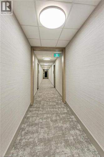 Corridor featuring patterned carpet, light wood-finish door frames, and flush-mount ceiling lighting - 2750 King Street E Unit# 103, Hamilton, ON 