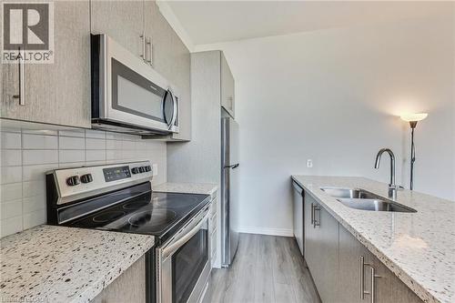 Modern kitchen featuring stainless steel appliances, speckled countertops, a tile backsplash, wood-finish flooring, and light-toned cabinetry - 2750 King Street E Unit# 103, Hamilton, ON 