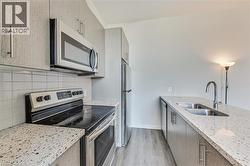 Modern kitchen featuring stainless steel appliances, speckled countertops, a tile backsplash, wood-finish flooring, and light-toned cabinetry - 