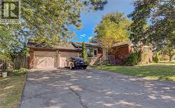 Brick facade residence featuring a two-car garage with carriage-style doors, a wide paved driveway, and mature trees providing shade - 