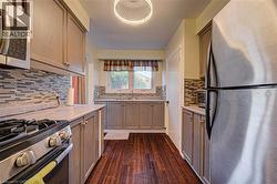 Galley kitchen featuring wood-finish flooring, light-toned cabinetry, light-toned countertops, a mosaic tile backsplash, and stainless steel appliances - 