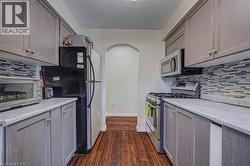 Galley kitchen featuring gray cabinetry, wood-finish flooring, a tile backsplash, and an arched doorway - 