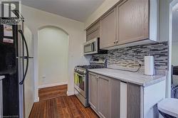 Kitchen featuring wood-finish flooring, light-toned cabinetry, a mosaic tile backsplash, and stainless steel appliances - 
