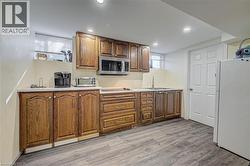 Kitchenette featuring wood cabinetry, light-toned countertops, a stainless steel microwave, and wood-finish flooring - 