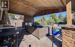 Covered outdoor patio featuring a wood-panel ceiling, stone-clad support pillars, and paver flooring - 