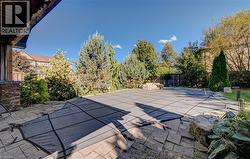 Expansive paved patio with a covered pool area, surrounded by mature trees and shrubs, featuring natural stone accents - 