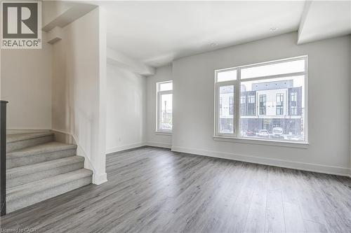 Spacious room with wood-finish flooring, large windows, and neutral carpeting on the staircase - 58 Windward Drive, Grimsby, ON 