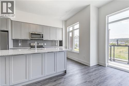 Kitchen featuring gray cabinetry, stainless steel appliances, a tile backsplash, light-toned countertops, and wood-finish flooring - 58 Windward Drive, Grimsby, ON 