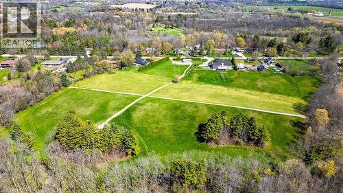 Expansive green field surrounded by mature trees, with a visible dirt path - 47 River Road, Brantford, ON 
