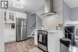 Kitchen featuring stainless steel appliances, light wood-style floors, white cabinetry, decorative backsplash, and glass fronted cabinets - 