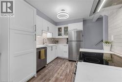 Kitchen featuring stainless steel appliances, exhaust hood, white cabinetry, light wood finished floors, and decorative backsplash - 