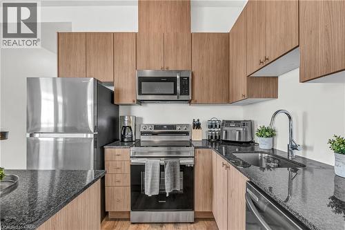 Kitchen featuring dark stone counters, stainless steel appliances, light wood-style floors, and modern cabinets - 460 Gordon Krantz Avenue Unit# 601, Milton, ON 