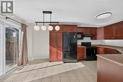 Kitchen featuring cherry wood-finish cabinetry, black appliances, light-toned tile flooring, and a sliding glass door - 
