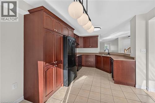 Full kitchen with wood-finish cabinetry, black appliances, and neutral tile flooring - 103 Emick Drive, Ancaster, ON 