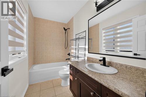 Bathroom featuring a white bathtub with tile surround, a dark wood-finish vanity with a single sink, and a large wall-mounted mirror - 103 Emick Drive, Ancaster, ON 